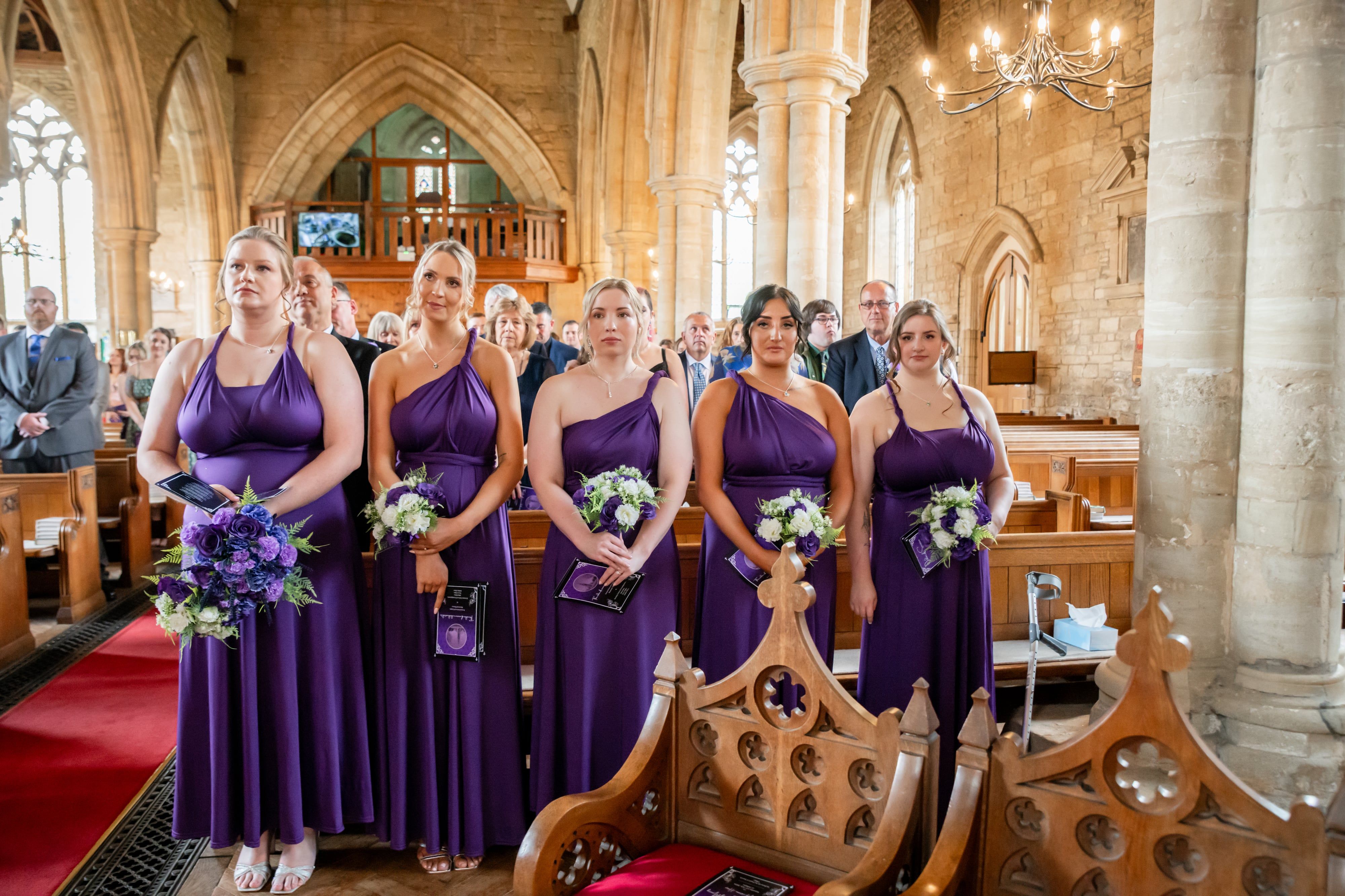 Five bridesmaids in purple stand for the hymn between the stone pillars