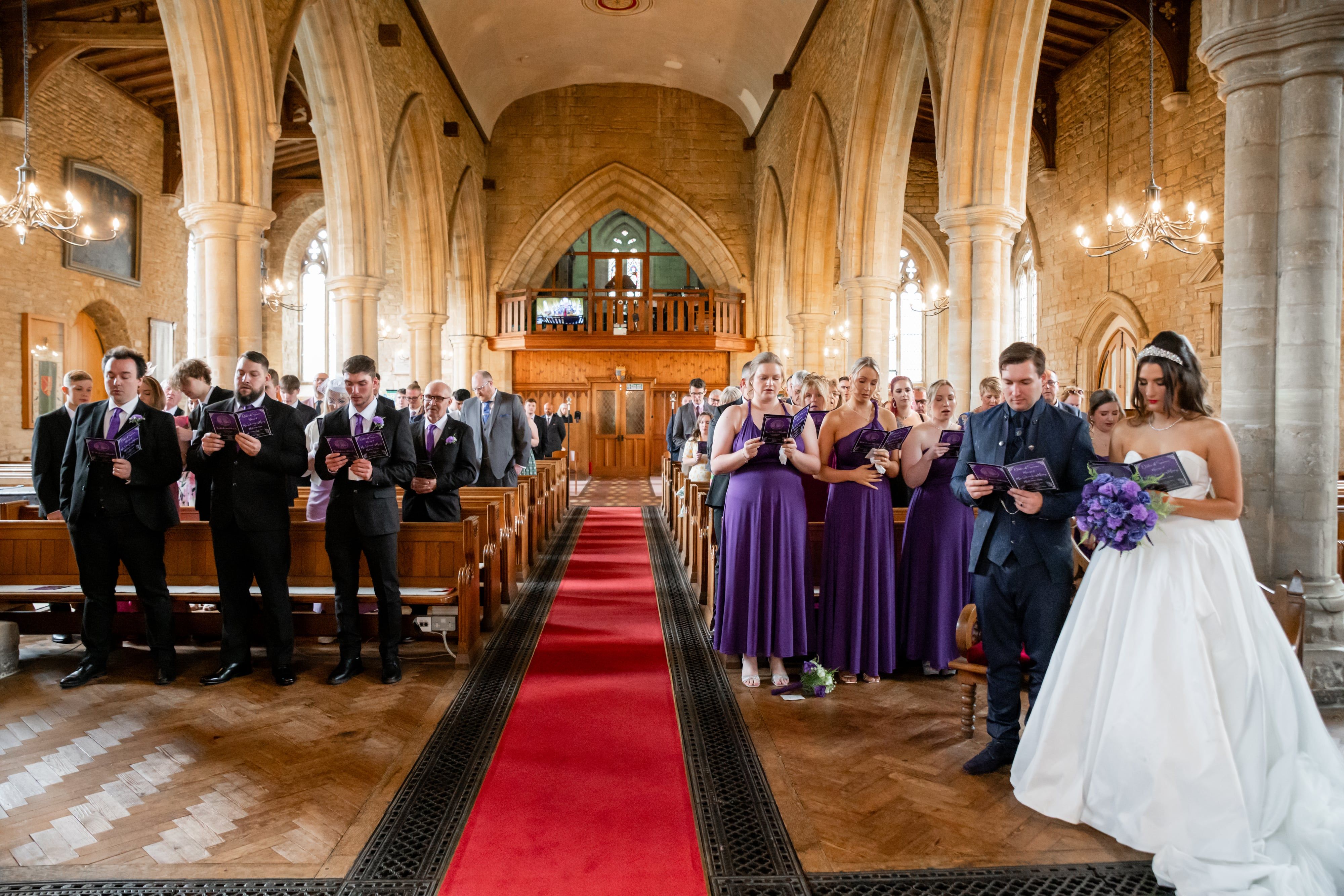 Congregation sings as the bride and groom stand at the head of the red-carpet aisle