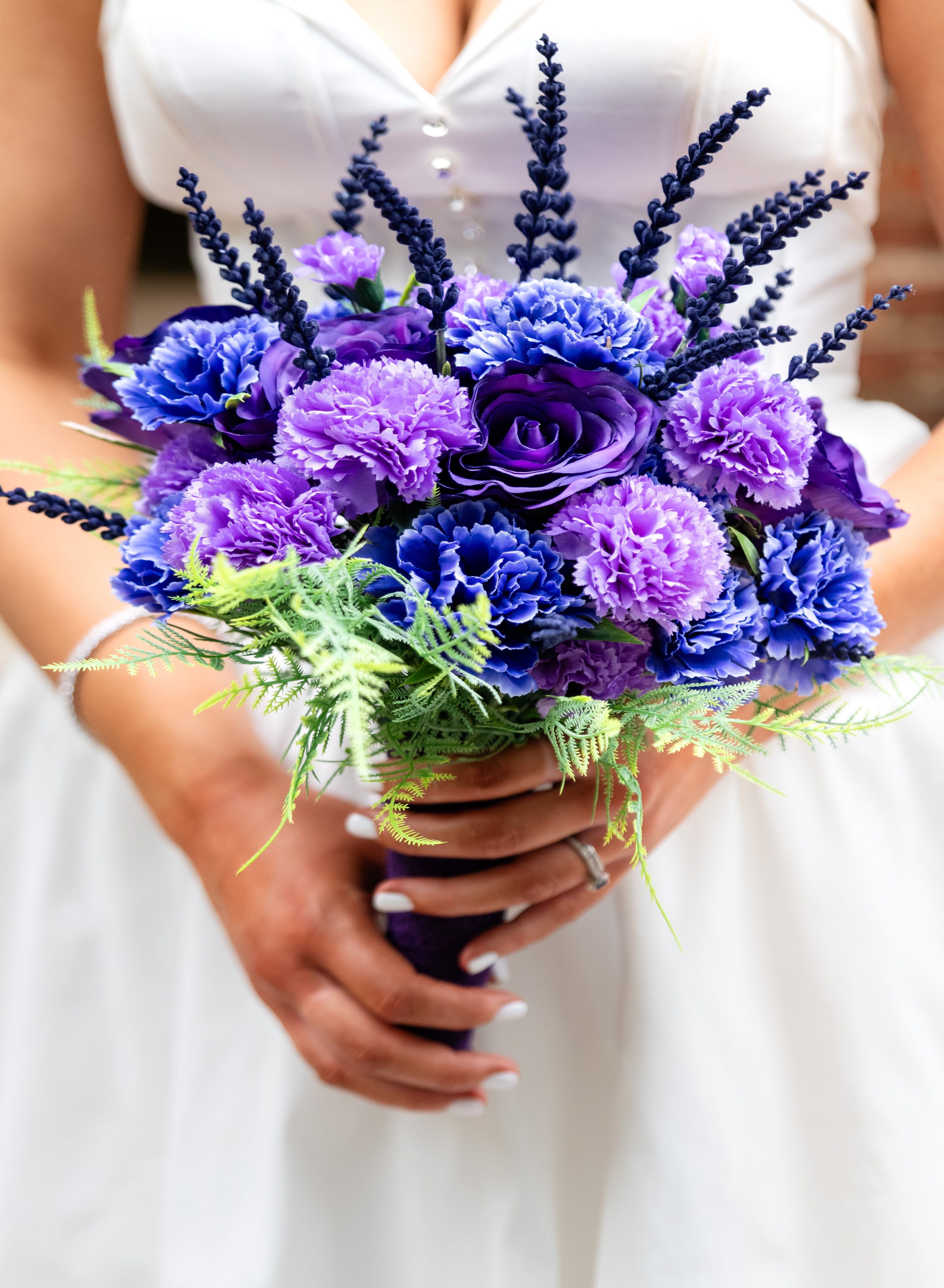 Purple carnation and lavender bouquet held against the white gown