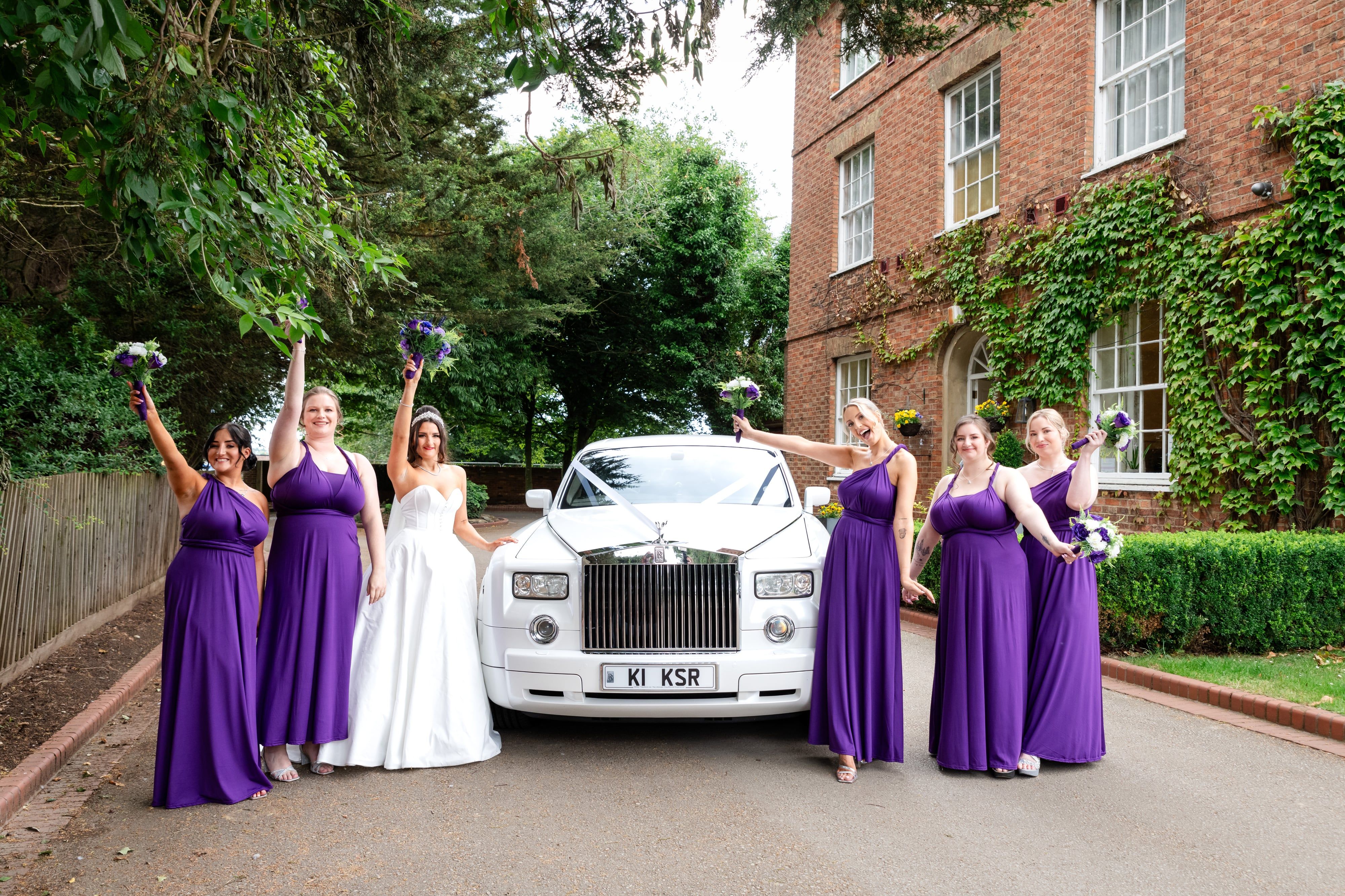 Bridesmaids raise their bouquets around a white Rolls-Royce outside Holiday Inn Milton Keynes East