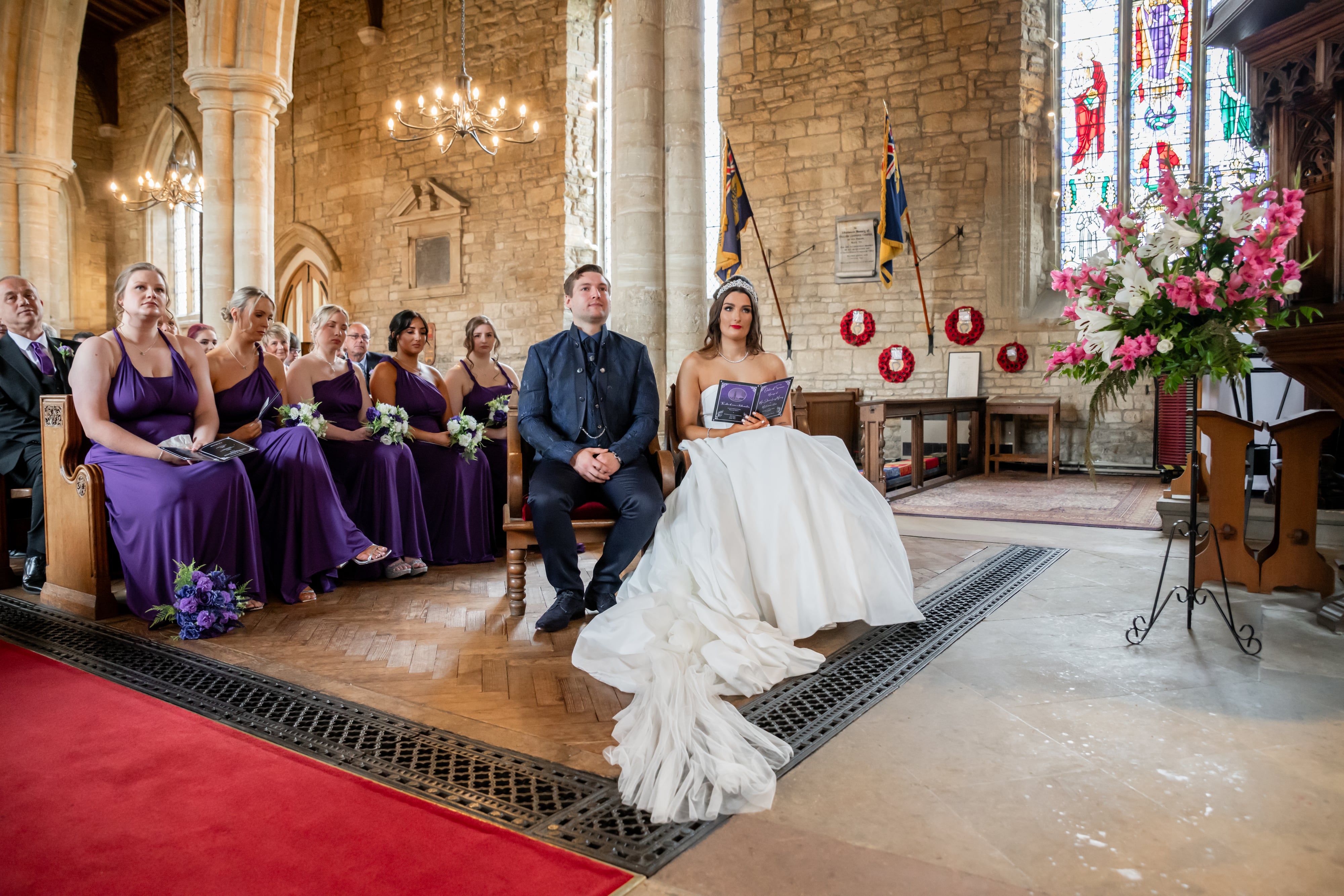 Bride and groom seated at the chancel, war memorial poppies on the stone wall behind