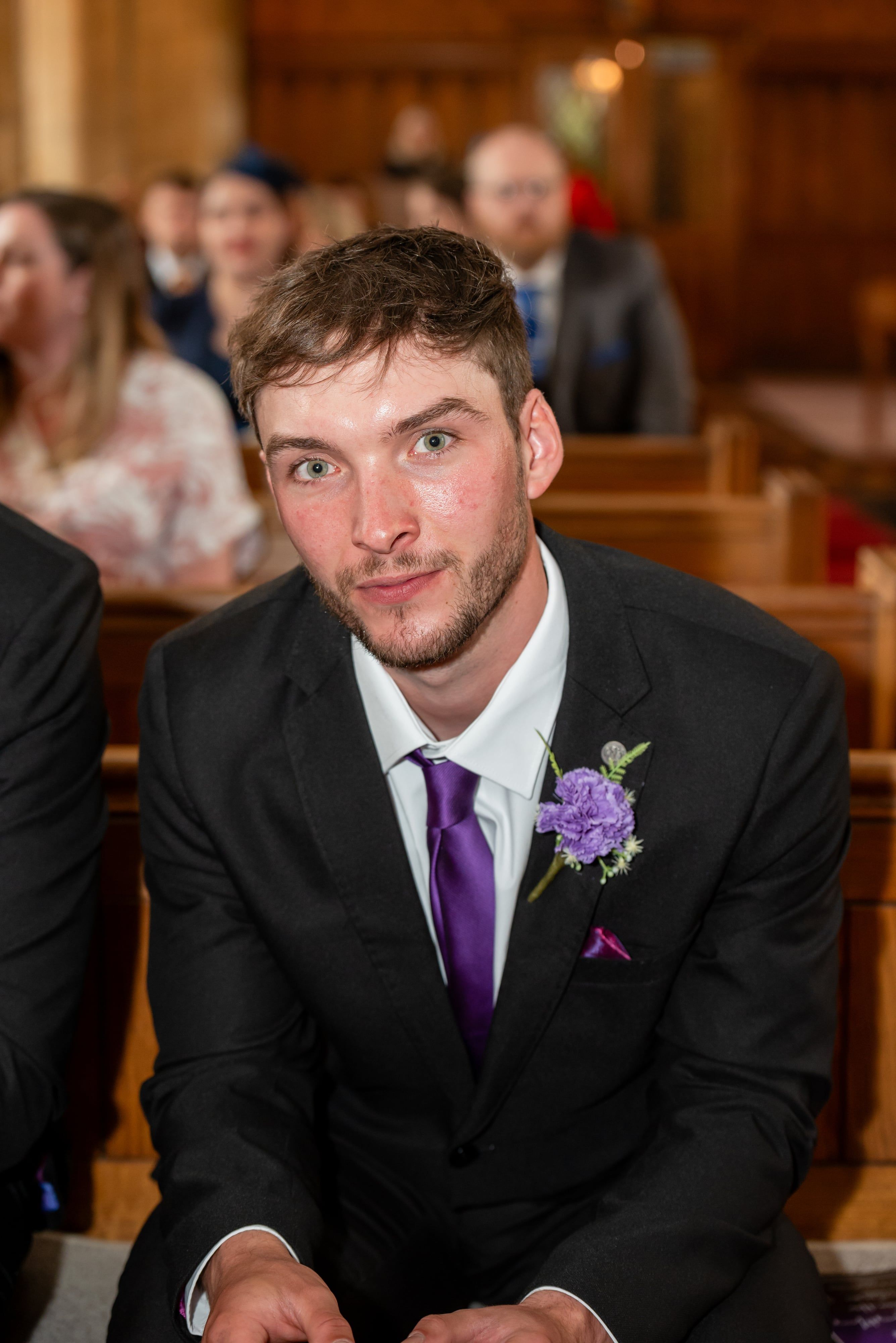Young groomsman with purple tie and buttonhole in the pews