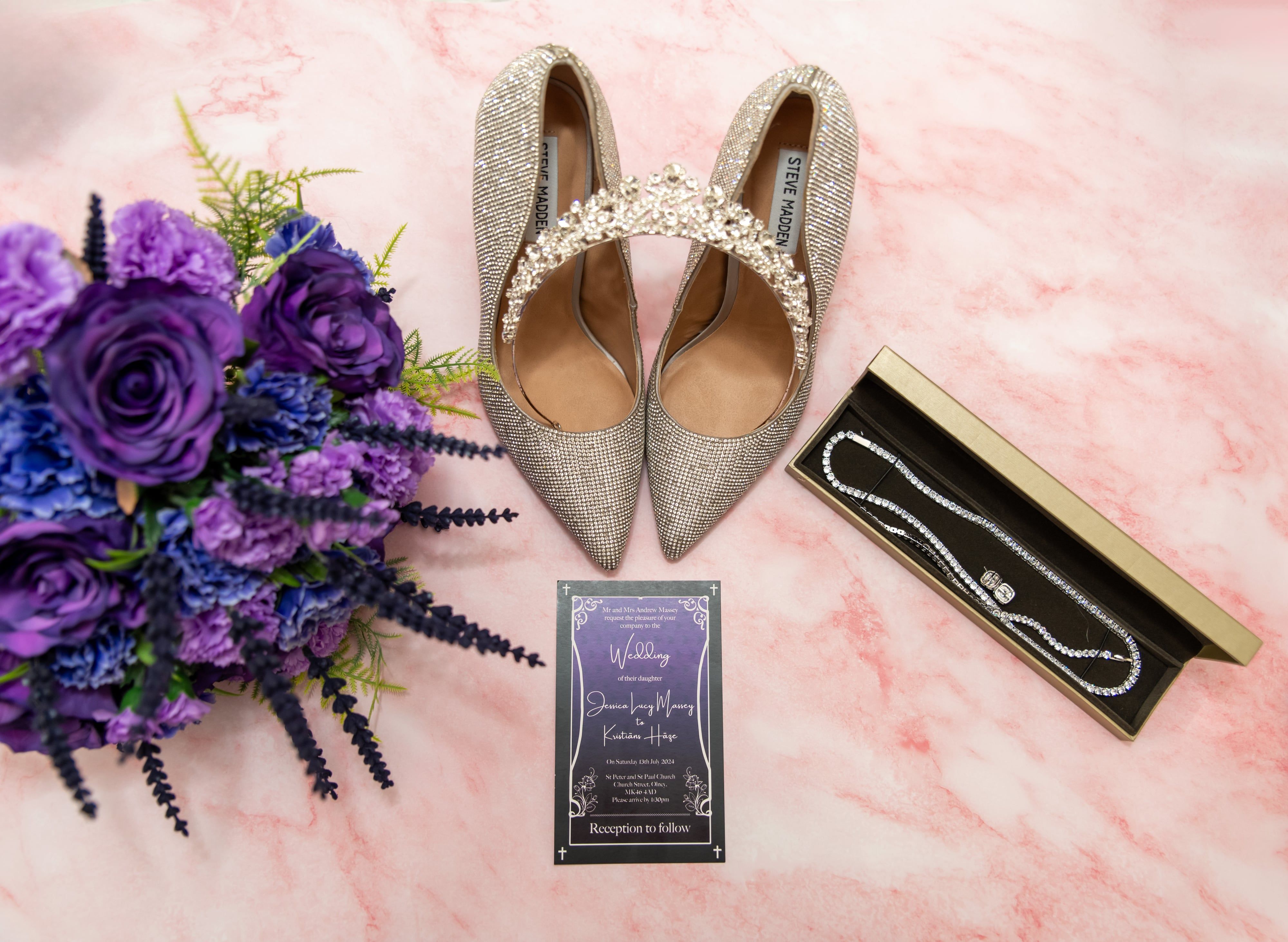 Sparkling heels, tiara, necklace and purple bouquet arranged around the wedding invitation